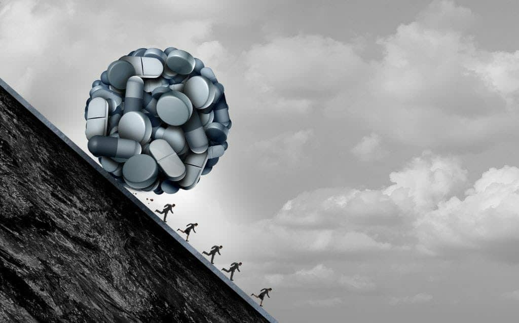 Several people flee a large ball of pills rolling downhill.